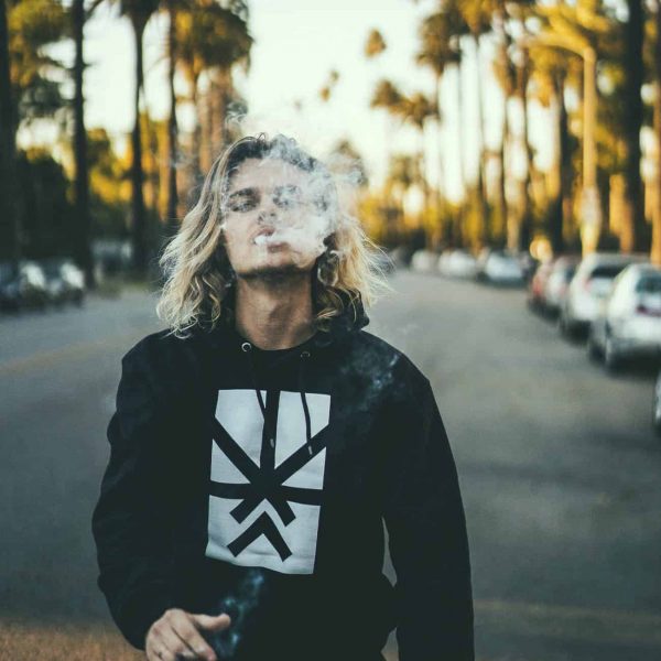 A man posing with a Project Cannabis Los Angeles hoodie blowing smoke