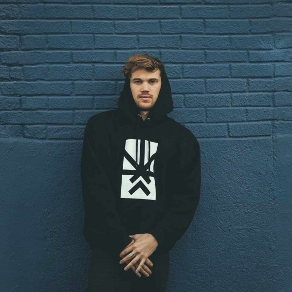 A man posing with a Project Cannabis Los Angeles hoodie against a wall