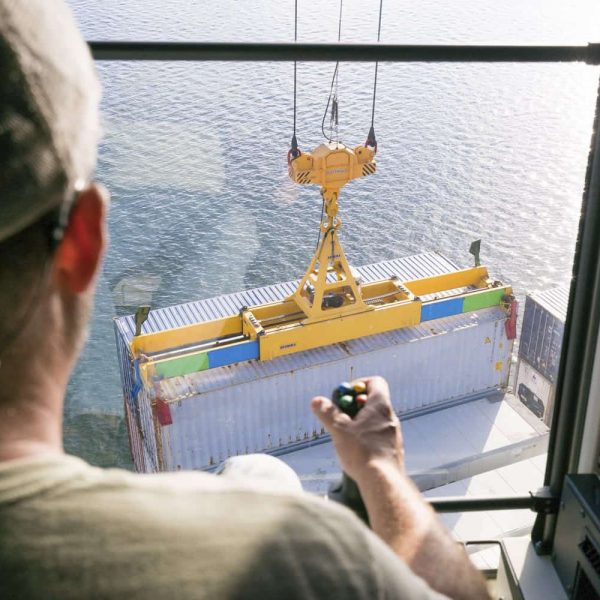 A man maneuvering a crane to lift a container out of a ship